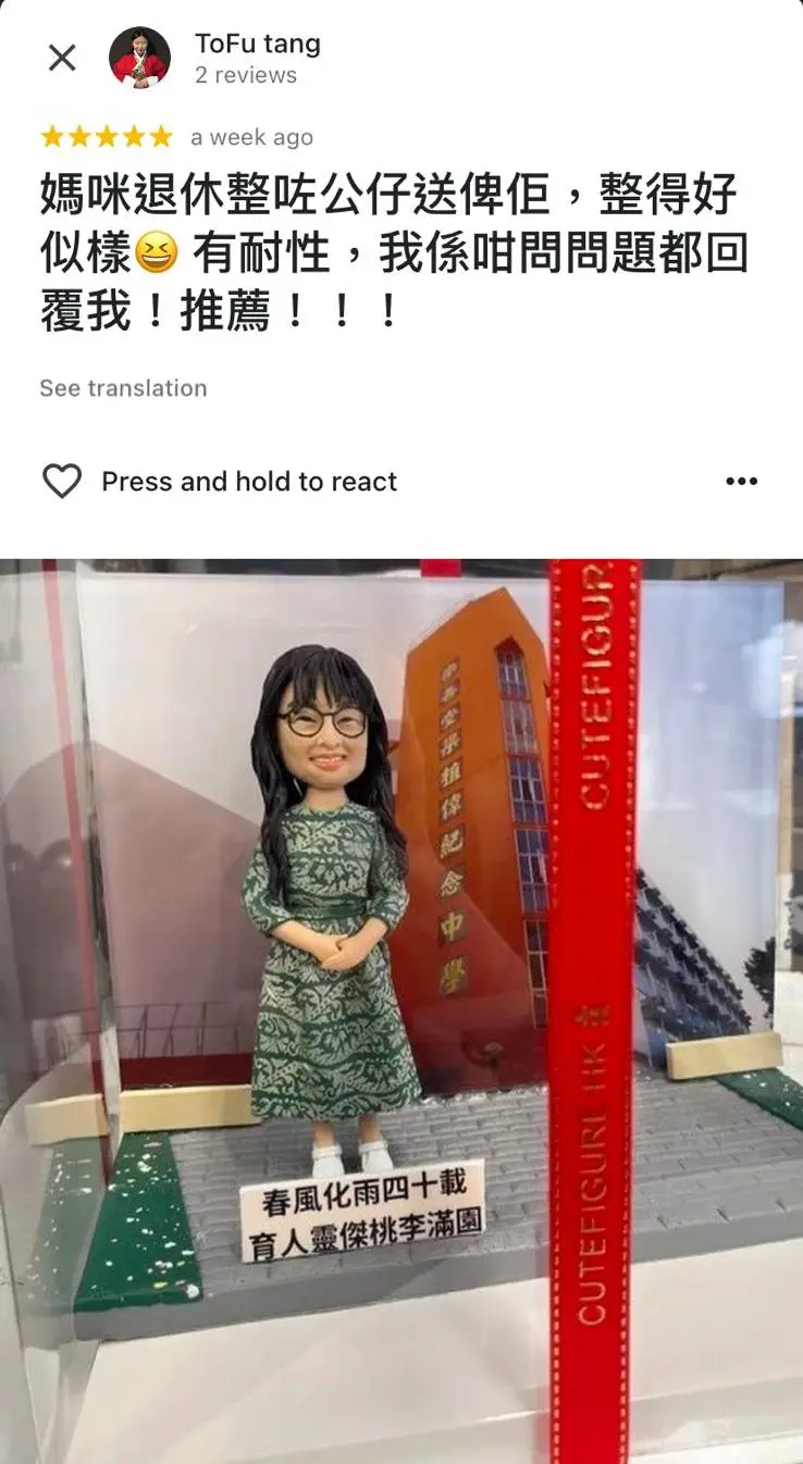 一尊為退休女教師訂製的人像公仔。公仔面帶微笑,身穿綠色連身裙,背景是她的學校建築,前方牌匾寫著「春風化雨四十載,育人靈傑桃李滿園」,是一份充滿敬意的榮休禮物。