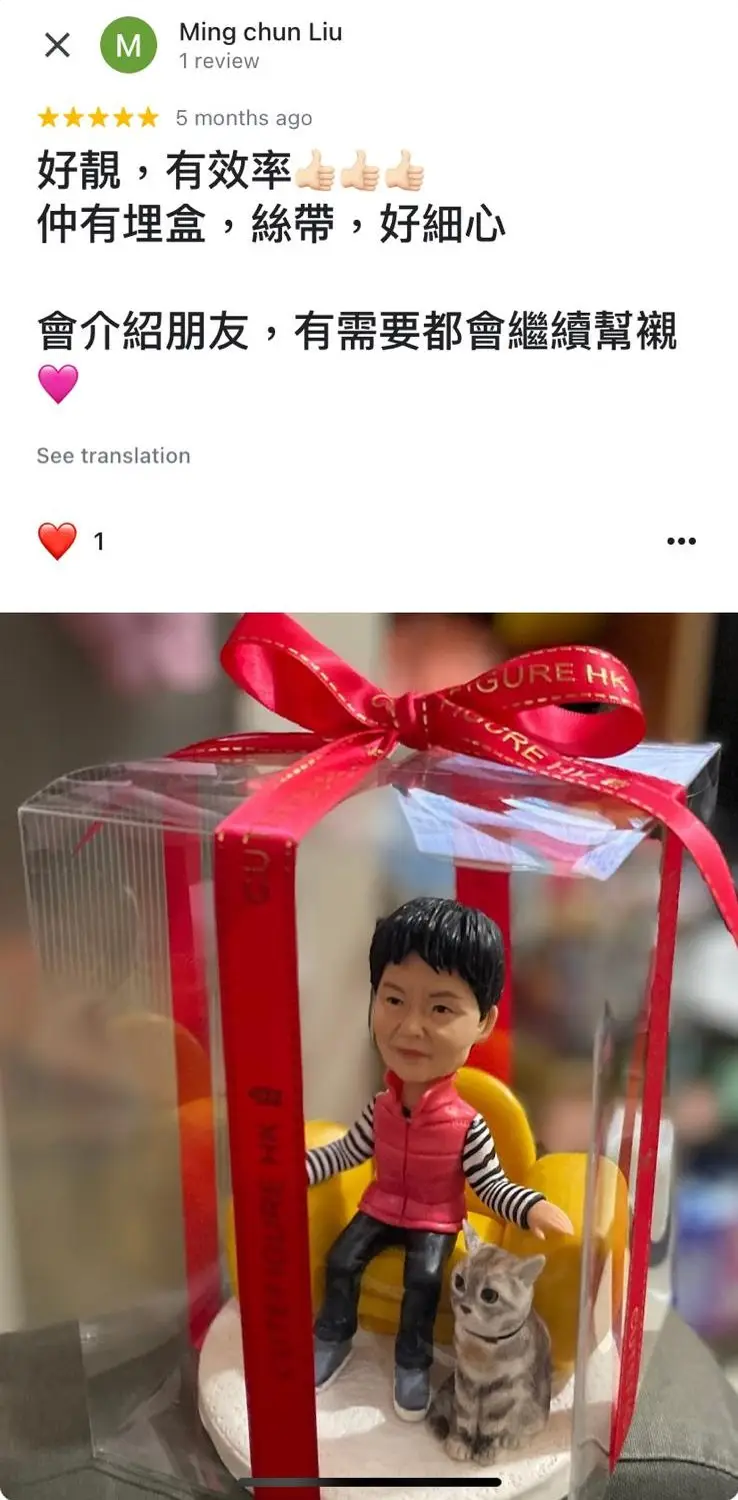 一件送給女士的上司退休禮物。一個短髮女士人像公仔,穿著紅色背心和黑白間條上衣,悠閒地坐在黃色沙發上,身旁還有一隻可愛的虎斑貓公仔。整個作品用透明禮盒和紅色絲帶精心包裝,充滿溫馨感。