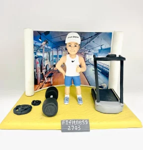一位健身教練的人像公仔，他在一個微縮的健身室場景中做出讚好手勢。場景中有跑步機和啞鈴，背景是健身室照片，名牌寫著「FT Fitness 2703」，是一份專業的健身禮物。