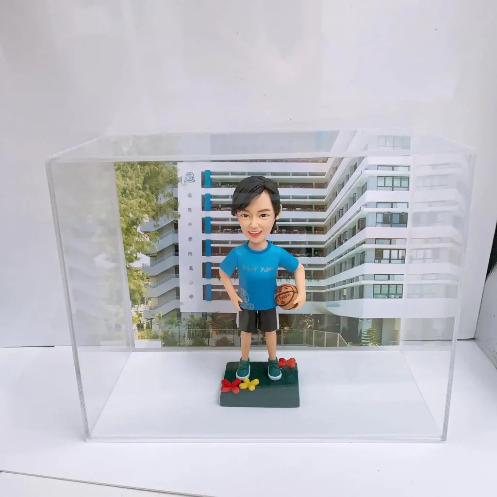 一位男士的榮休禮物人像公仔，他拿著籃球，站在以校園建築為背景的陳列盒中，是一份送給老師或教練的禮物。