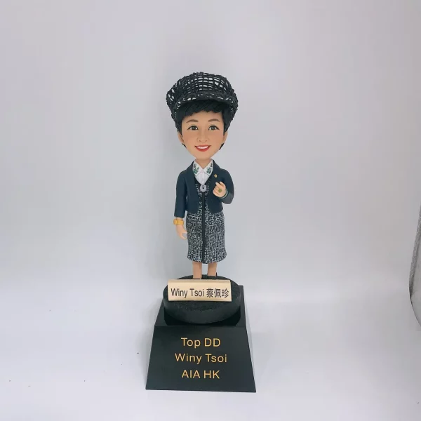 一款為AIA保險公司Top DD Winy Tsoi訂製的人像公仔獎盃，公仔頭戴貝雷帽，身穿時尚套裝，站立在刻有其姓名和榮譽頭銜的黑色獎盃底座上。