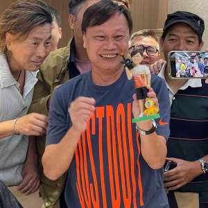 一張香港TVB演員在一眾好友的簇擁下，開心收到自己專屬人像公仔的照片。他高舉著這個根據他樣貌訂製、手持攝影機的人像公仔，笑容燦爛。這份禮物完美展現了送給tvb演員的創意與心意。