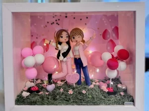 白色相框中的粉紅派對場景：兩位女孩造型的Q版公仔並肩擺姿勢，一位穿粉色運動套裝配黑色斜背包，另一位穿粉色外套與牛仔褲，背景有粉紅與白色氣球、星星點綴與暖白燈串，草地上散落小花與愛心裝飾。