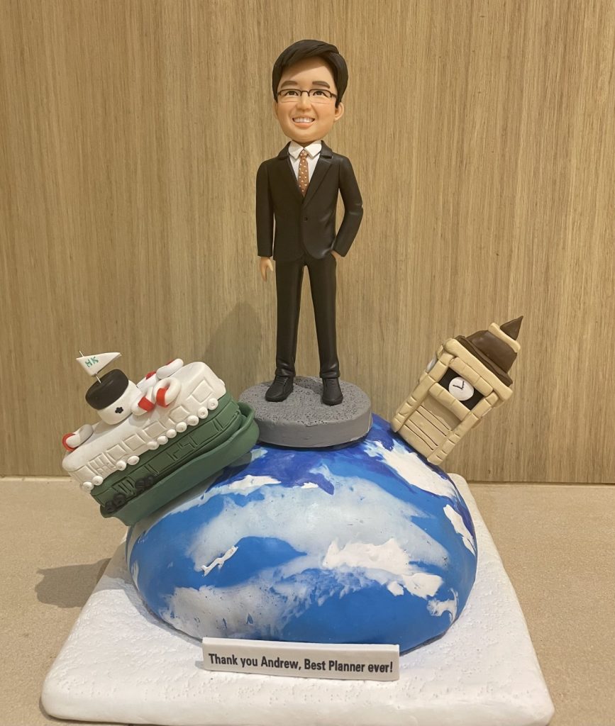 一位男性人像公仔穿著西裝，站在地球造型底座上，周圍有英國大笨鐘和遊輪裝飾