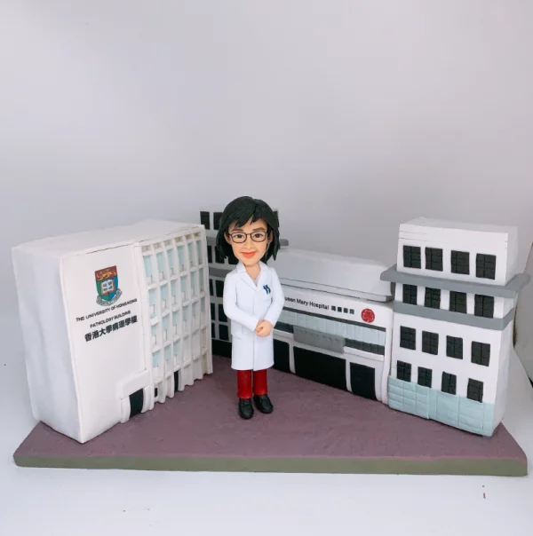 身穿醫生袍的Q版真人公仔，站在香港大學病理學樓和瑪麗醫院模型前，是送給醫護人員的訂造人像公仔。