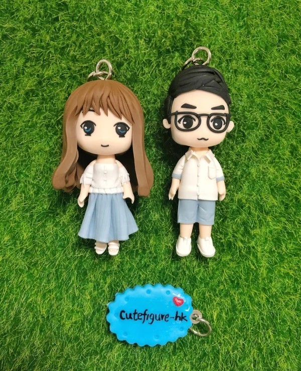 一對穿著休閒服飾的Q版真人公仔情侶鎖匙扣，女生公仔穿白色上衣和藍色裙，男生公仔穿白色襯衫和藍色短褲，是送給情侶的訂造人像公仔禮物。