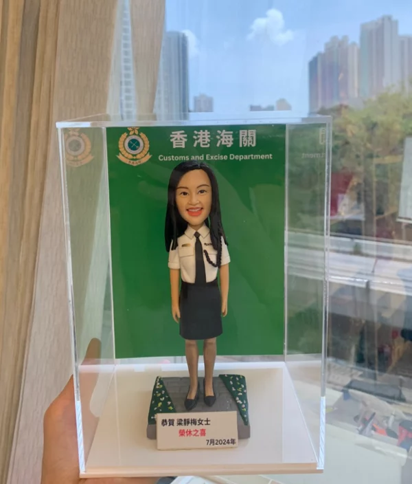 身穿海關制服的Q版真人公仔，背景是香港海關標誌，底座寫有「恭賀 梁靜梅女士 榮休之喜 7月2024年」，是送給海關人員的訂造退休禮物。