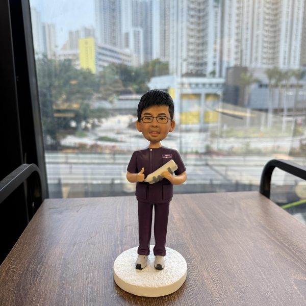 一位身穿紫色制服的男性牙醫人像公仔，他面帶微笑，一手拿著牙齒模型，另一手做出「讚好」手勢，背景為城市景觀，是一份表彰其專業技術的榮休禮物。