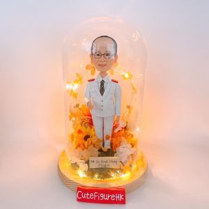 一款為Lo Kwok Hung醫生量身訂製的醫生人像公仔，作為一份榮譽禮物，被精心放置在一個帶有LED燈的玻璃罩中，並以向日葵等黃色永生花作為裝飾，注定會獲得客人好評(CM)。
