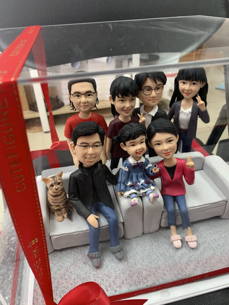 七位家庭成員和一隻貓的人像公仔坐在沙發上，大家面帶笑容，姿勢自然，展現大家庭的溫馨氣氛。