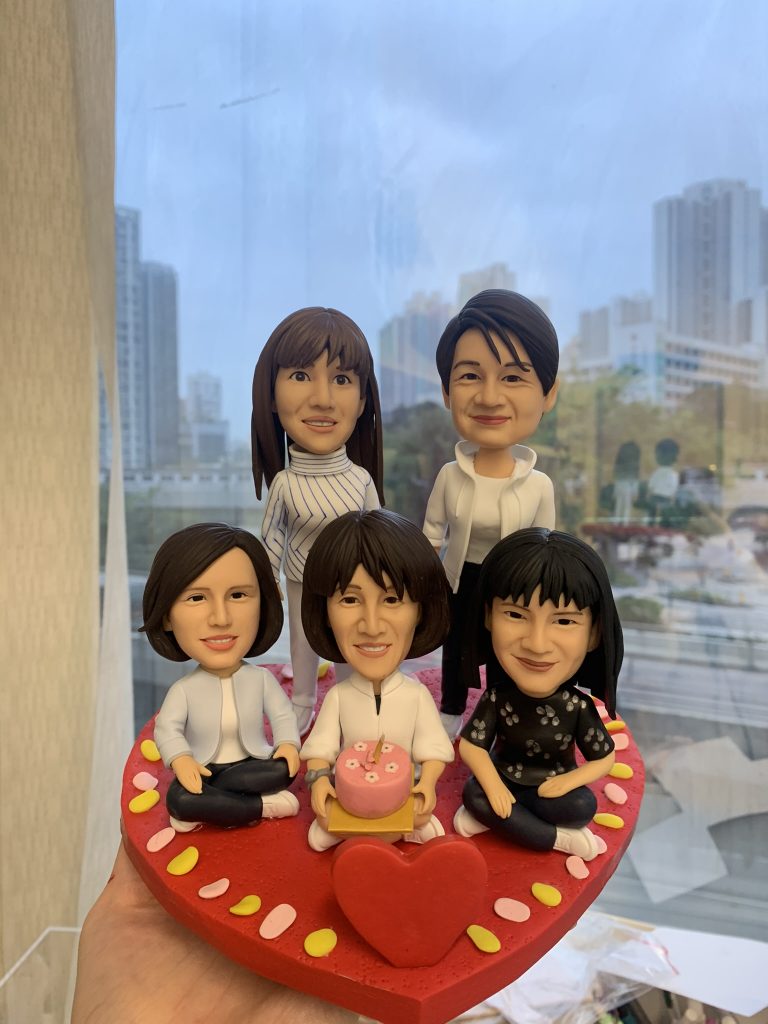 五位女性人像公仔坐在紅色心形底座上，其中一位手持生日蛋糕，背景為窗外城市景色，展現生日聚會的歡樂氣氛。