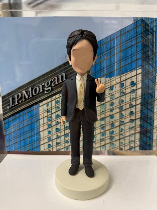 一款贈予J.P. Morgan員工的人像公仔，公仔身穿西裝並做出V字手勢，背景是J.P. Morgan的公司大樓。這是一款象徵專業與成就的企業歡送禮物。