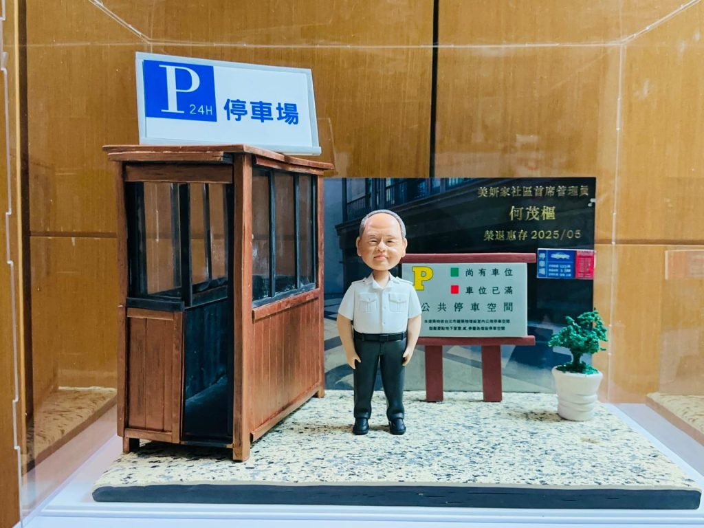 一個以停車場為主題的人像公仔退休禮物。公仔站在仿真崗亭旁,背景有「P 24H 停車場」標誌、公告牌顯示車位資訊、綠色盆栽,以及標有名字和榮休日期的金色牌匾,細緻還原退休人士的工作環境。
