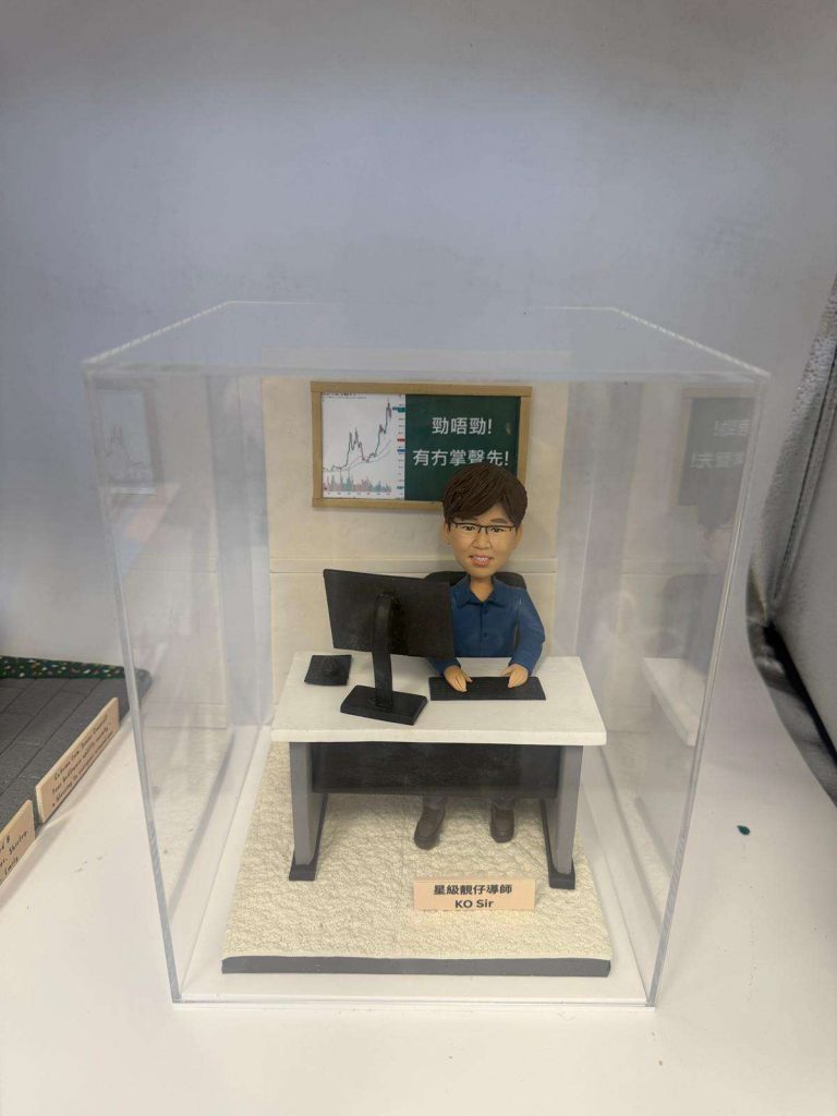 一款為「星級靚仔導師 KO Sir」量身訂製的人像公仔，他是教育界的權威代表。公仔場景還原了他坐在辦公桌前的風采，背景板上是股票圖表和他的教學金句，是一款極具份量的致敬禮物。