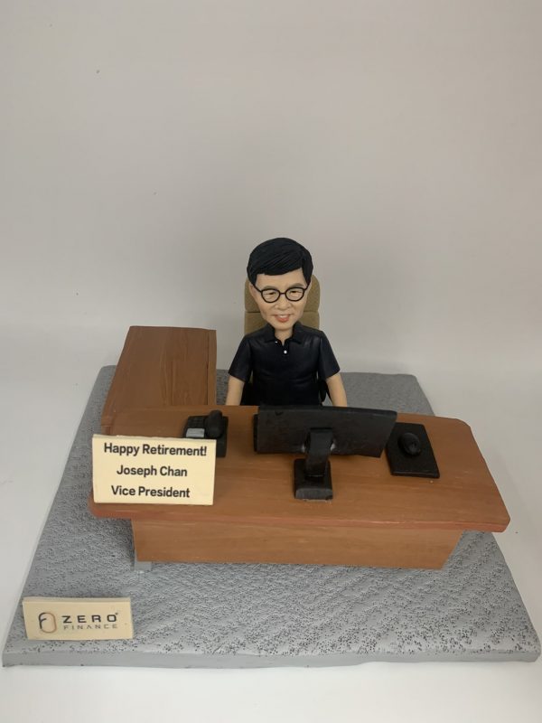 一件為ZERO FINANCE公司副總裁 Joseph Chan 訂製的人像公仔榮休禮物。公仔主角戴著眼鏡，面帶微笑地坐在木紋辦公桌前。桌上有名牌寫著『Happy Retirement!』及他的職位，底座上則有ZERO FINANCE的公司標誌。
