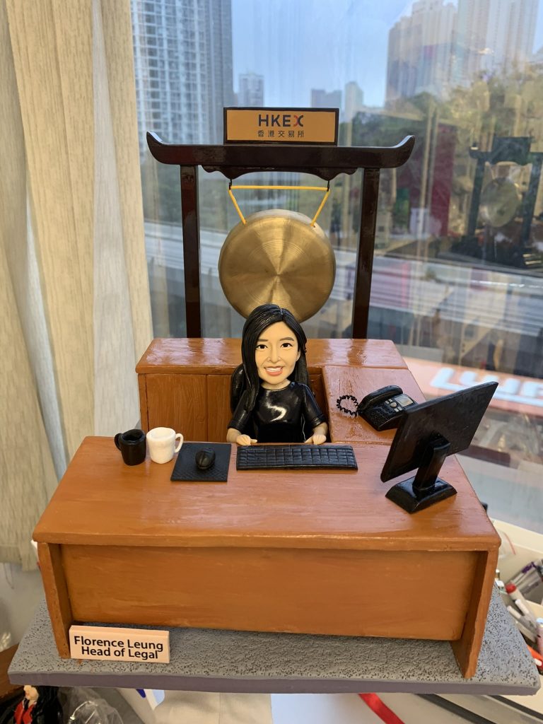 一件極具氣勢的女性上司榮休禮物。一位女性人像公仔坐在行政辦公桌前，最矚目的背景是她身後一座巨大的中式銅鑼，象徵著為她輝煌的職業生涯「鳴金收兵」、功成身退。整個場景設置在能看到城市高樓景觀的窗前，彰顯其高階主管的地位。