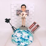 一款客製化的企業高層退休禮物，一位男士人像公仔站在地球模型上，場景包括專業攝影機、立體建築模型以及印有公司logo的背景牆，呈現全球領導者的風範。