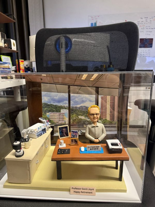 訂製醫生人像公仔｜教授坐於辦公桌前，桌面擺放電腦滑鼠、筆、紙張與個人照片，背景還原窗外大學醫院景觀，桌邊配有醫療監測儀器與實驗設備，展現醫護專業氛圍與退休紀念禮物的獨特價值。