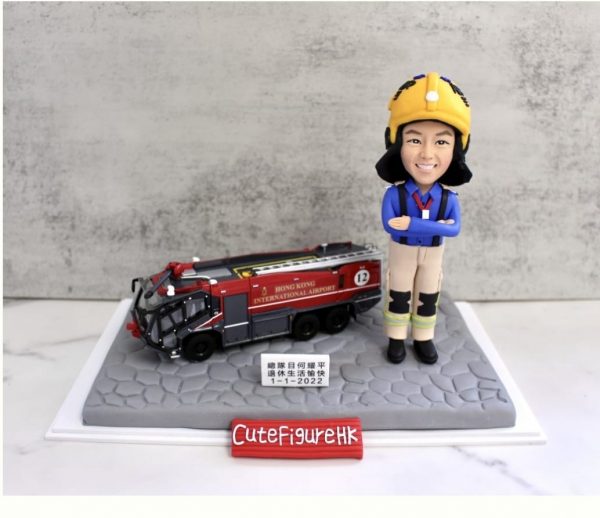 一款為機場消防員訂製的退休人像公仔，公仔身穿全套消防制服，旁邊停放著一輛香港國際機場的專用消防車模型，底座銘牌刻有贈予總隊目何耀平的退休祝福。