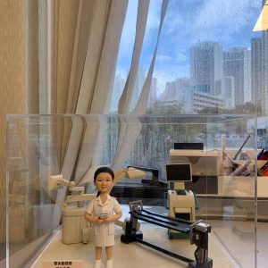 護士人像公仔，身穿白色制服，手持文件，站在醫療手術室場景中。背景包含手術燈、醫療監測儀與手術台等專業醫療設備，整體設計逼真，象徵醫護人員的專業與關懷。此公仔是專為醫生或護士設計的客製化禮物，適合作為醫護感謝、升職或退休紀念。