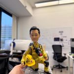 一款訂製的消防人像公仔，呈現出英雄般的單膝跪地姿勢。公仔身穿全套黃金戰衣，手持寫有「TST」的黃色頭盔，站立在石磚底座上，是一份極具紀念價值的退休禮物。