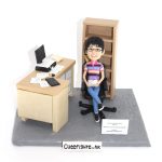 一座辦公室情境的人像公仔：短髮戴眼鏡的人物穿著粉紫綠條紋POLO衫與牛仔褲，坐在黑色旋轉辦公椅上，手持文件微笑。右後方是淺木色高書架，左側是一張L形工作桌，上有開啟的筆記型電腦、印表機/文件匣、開本書籍、散落紙張、黑色計算機與滑鼠。整體置於灰色地台上，前方立有小牌寫著感謝與服務年資字樣，呈現溫馨的職場致敬氛圍與寫實文書細節的人像公仔作品。