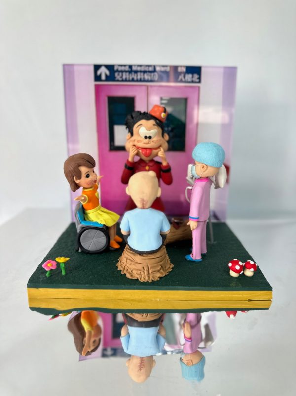 兒科病房場景中的醫生與醫護人像公仔：背景是醫院兒科病房入口（兒科病科病房 / Paed. Medical Ward），場景中有一位戴藍色手術帽、身穿粉紅制服的醫護公仔，陪伴兩位小病童──一位坐輪椅的小女孩、一位頭上有手術疤痕的男孩；中央則有一位扮小丑的表演者，用誇張表情逗笑病童。展示盒細節包含花朵、紅白蘑菇裝飾，呈現出溫馨療癒氛圍，適合作為醫生醫護主題的禮物或紀念公仔。