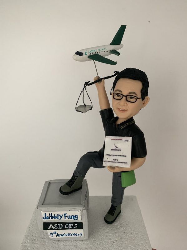 一款為國泰航空地勤營運人員訂製的15週年紀念人像公仔，主角手持飛機裝卸手冊，並舉著一個帶有飛機模型與天秤的背景配件裝飾。