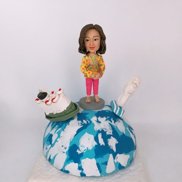 一款送給外國同事的退休禮物，一位女士人像公仔站在地球模型上，地球上有香港的天星小輪模型和新加坡的魚尾獅模型，象徵著兩地的美好回憶。