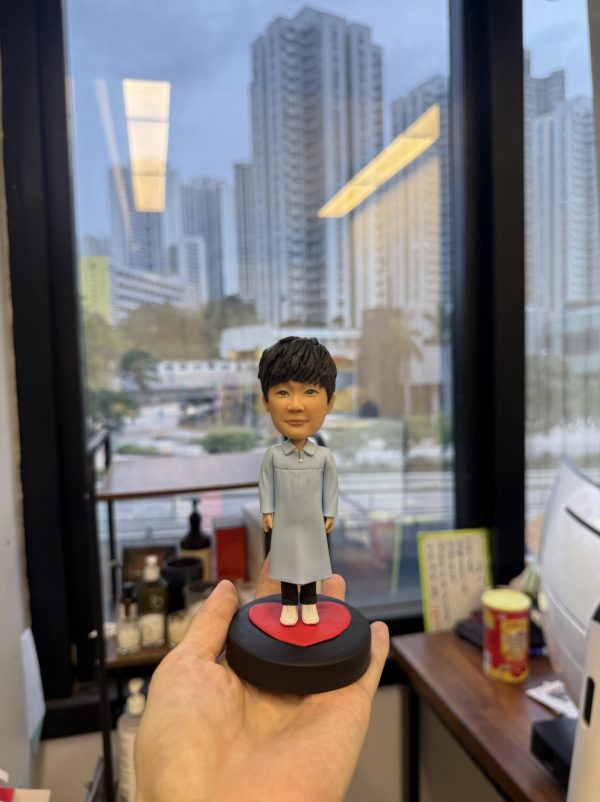 單人宗教人像公仔立於黑色圓形底座上的紅色愛心平台：公仔穿淡藍長袍、深色長褲與白色球鞋，短黑髮、微笑神情。整體造型清新，適合作為洗禮禮物或信仰紀念的人像公仔。