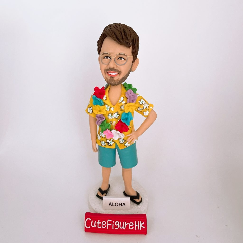 一款為外國同事訂製的人像公仔禮物,公仔是一位戴眼鏡的男士,穿著黃色夏威夷襯衫和戴著花環,站在一個寫有「ALOHA」的沙灘造型底座上。