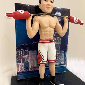 一款客製化人像公仔，公仔展現健身運動姿態，赤裸上身展現結實肌肉線條，身穿白色紅邊籃球短褲與黑色運動鞋，肩上扛著造型啞鈴，背景是香港夜景大樓燈光，象徵力量、運動與專屬紀念的結合。