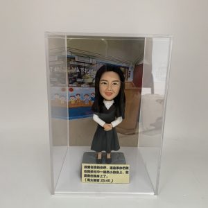 一款放置在透明亞加力膠盒中的客製化女士人像公仔，底座刻有聖經經文，背景為教室，是一份送給主日學老師或傳道人的感謝禮物。