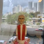 單人牧師人像公仔：身穿白色長袍外搭紅色聖帶，胸前有十字樣式與魚形圖案，黑框眼鏡、短白髮，表情穩重端莊；立於紅色心形底座，前方牌匾可客製祝福語與姓名。此人像公仔適合作為授職、榮休、探訪與感謝致贈的禮物。