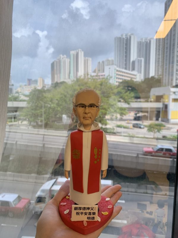 單人牧師人像公仔：身穿白色長袍外搭紅色聖帶，胸前有十字樣式與魚形圖案，黑框眼鏡、短白髮，表情穩重端莊；立於紅色心形底座，前方牌匾可客製祝福語與姓名。此人像公仔適合作為授職、榮休、探訪與感謝致贈的禮物。