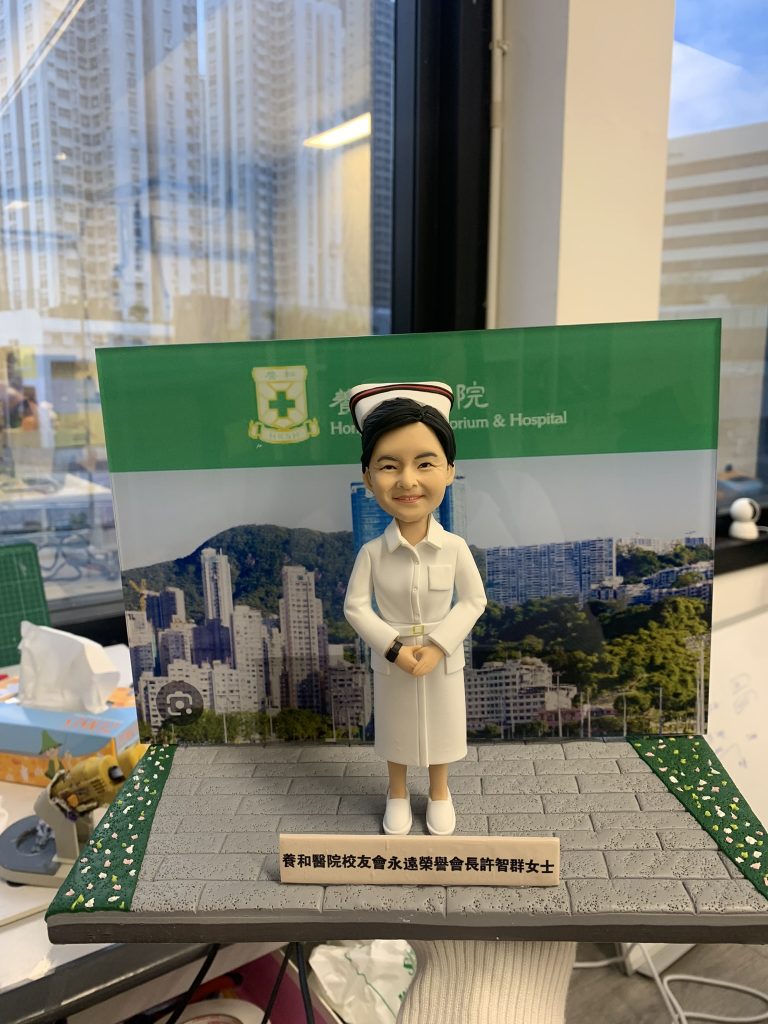 一份贈予養和醫院校友會永遠榮譽會長許智群女士的榮譽紀念禮物。精緻的人像公仔身穿護士長制服，莊重地站立在刻有其職銜的銘牌後方，背景板展示了養和醫院的標誌與面貌，是一份極具份量的退休禮物。