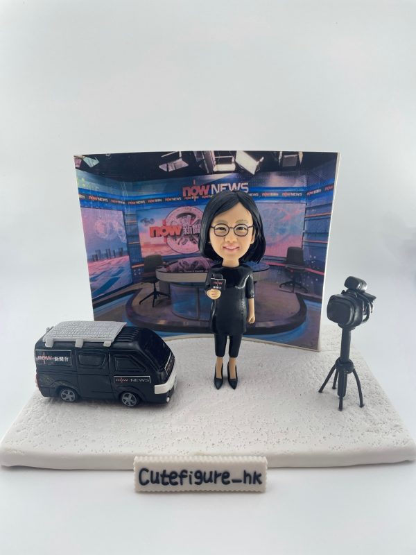 新聞採訪主題人像公仔場景：短髮戴眼鏡的女性記者穿黑色連身裙與高跟鞋，手持麥克風站在白色地台上；左側是一台黑色新聞採訪車模型，右側為架在三腳架上的專業攝影機；背板呈現演播室畫面與節目佈景。整體具專業與儀式感，適合作為新聞記者退休禮物與致敬紀念擺設。