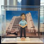 一款為香港女警員訂製的榮調紀念人像公仔，公仔身穿警察制服，背景為荔枝角收押所，由其同事為祝賀她調職而敬贈。