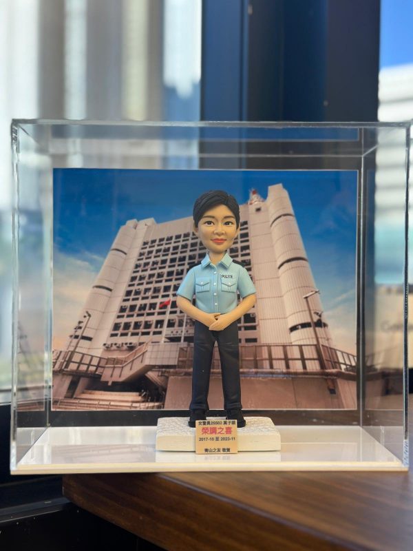 一款為香港女警員訂製的榮調紀念人像公仔，公仔身穿警察制服，背景為荔枝角收押所，由其同事為祝賀她調職而敬贈。