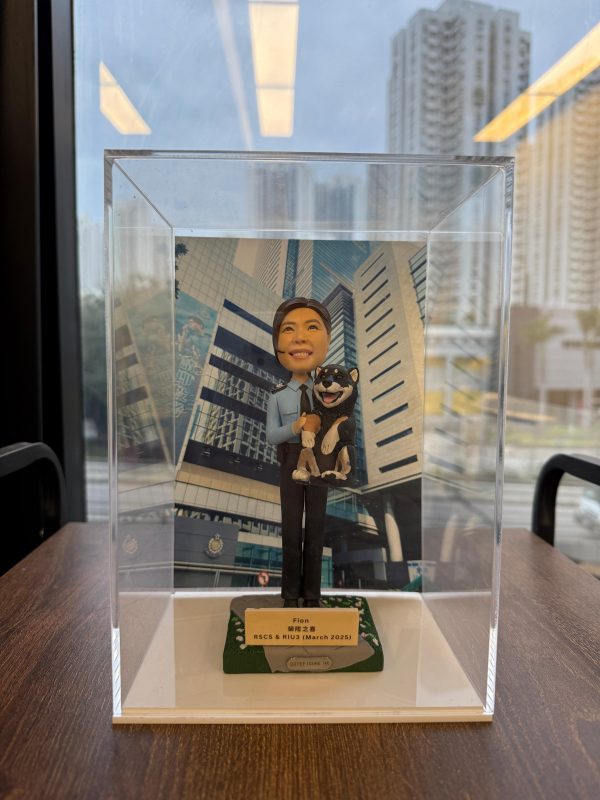 一款祝賀女警務人員晉升的人像公仔禮物，公仔身穿警察制服並懷抱一隻柴犬寵物，背景是警察總部大樓照片。底座銘牌記錄了這次晉升的職級與日期。