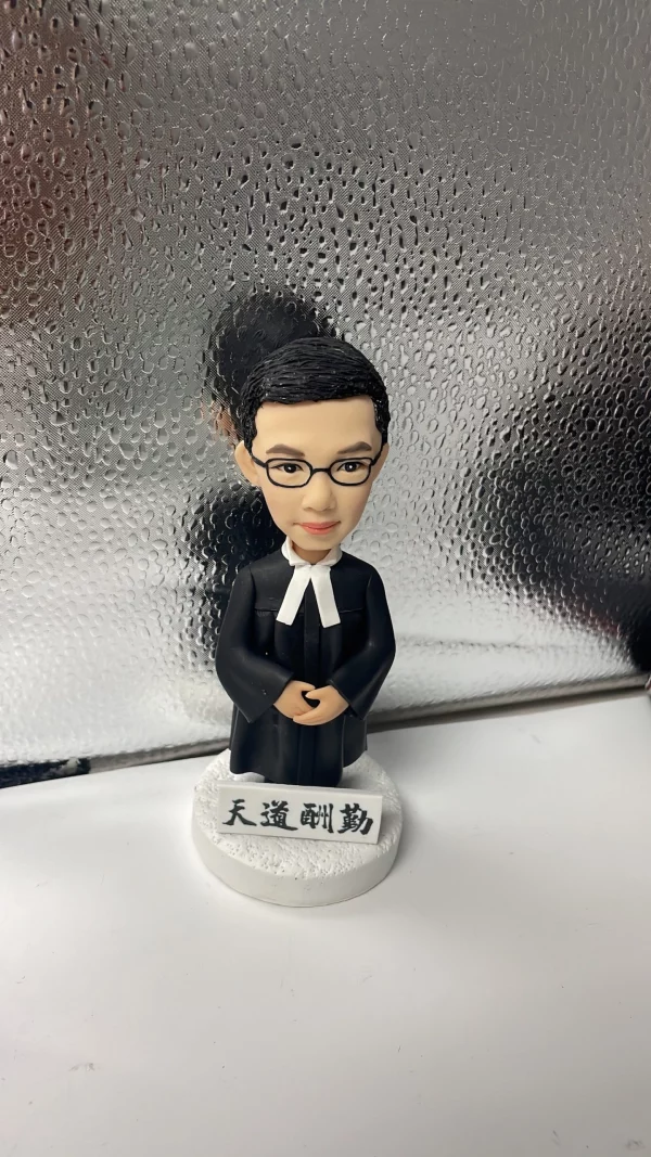 一款男性律師人像公仔，身穿律師袍，站立在刻有「天道酬勤」銘牌的底座上，是送給律師的完美入職禮物。