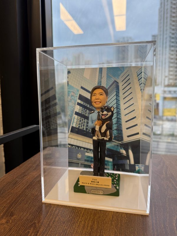 一款祝賀女警務人員晉升的人像公仔禮物，公仔身穿警察制服並懷抱一隻柴犬寵物，背景是警察總部大樓照片。底座銘牌記錄了這次晉升的職級與日期。