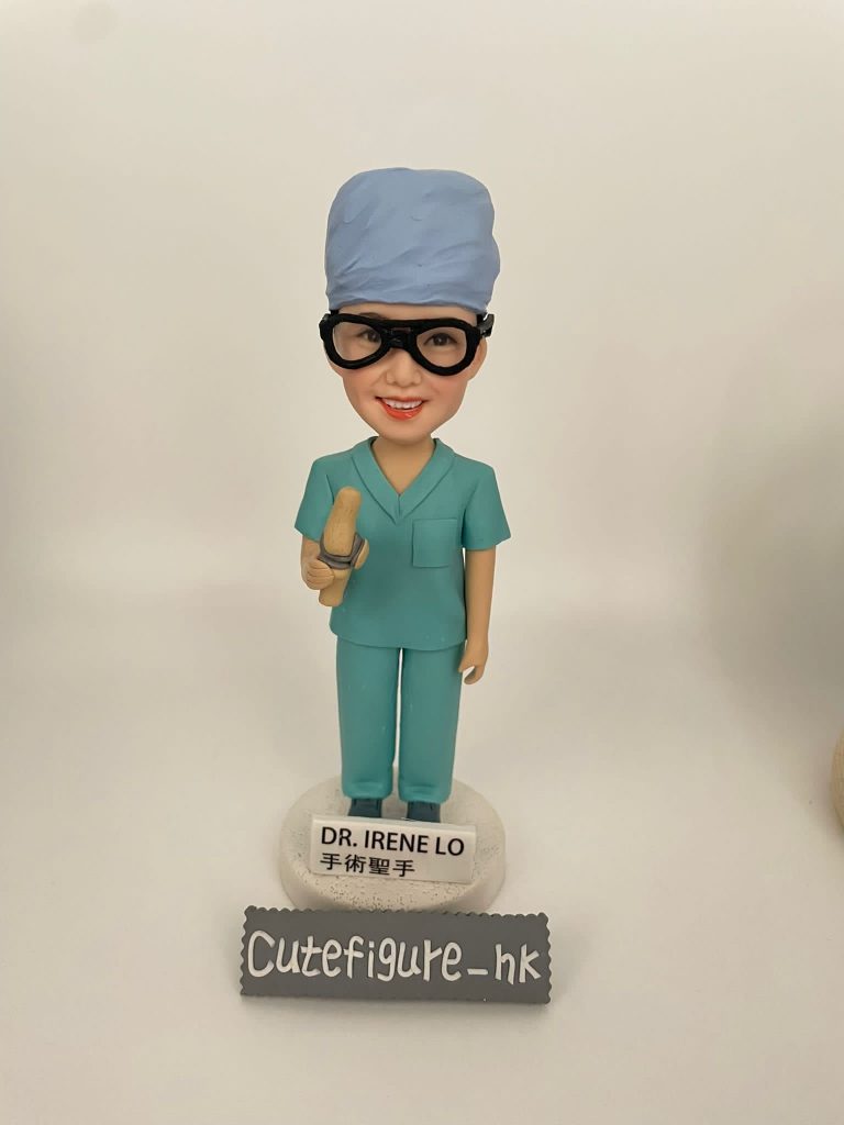 康復感謝醫生 定製醫生人像公仔,角色為外科醫生 Dr. Irene Lo,身穿綠色手術衣與手術帽,配戴護目鏡,手持手術工具,底座寫有「DR. IRENE LO 手術聖手」。此醫護公仔專為外科醫生設計,是獨特的醫療專屬禮物。
