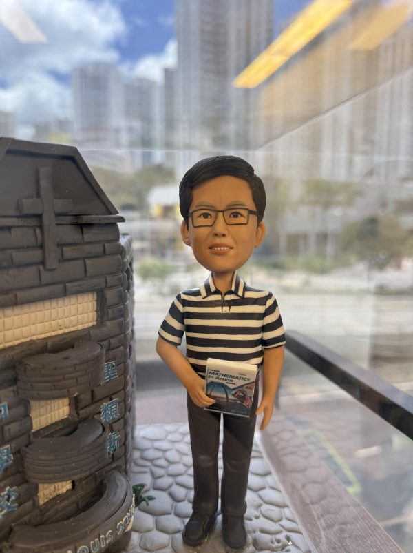 一款為聖類斯中學的黎德維校長（Mr. Lai Tak Wai）訂製的校長退休禮物。精緻的人像公仔手持數學書，莊重地站在一座細節豐富的聖類斯中學立體學校模型旁，底座前方陳列著五個社（LILY, ROSE, SHAMROCK, THISTLE, TULIP）的標誌，整件作品置於透明保護罩中，是一份極具份量的榮休紀念品。