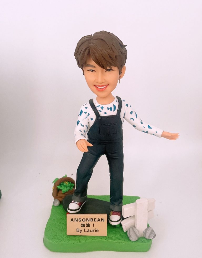 定制滑板公仔,短髮笑容造型,身穿黑色背帶褲與白色印花長袖上衣,站在綠色滑板造型底座上,旁邊有小籃與木牌裝飾,木牌寫有「ANSONBEAN 加油!By Laurie」。