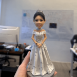 一款優雅的女歌手人像公仔，她頭戴皇冠，身穿一件銀白色碎花圖案的露肩晚裝長裙，姿態高貴地站立在灰色圓形地台上。