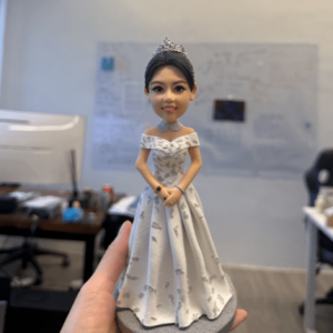 一款優雅的女歌手人像公仔，她頭戴皇冠，身穿一件銀白色碎花圖案的露肩晚裝長裙，姿態高貴地站立在灰色圓形地台上。