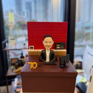 專為老闆與資深領袖打造的人像公仔，以辦公室實景為靈感：深棕色主管書桌、紅色背板、電腦螢幕與鍵鼠、文件抽屜等細節完整重現，並加入「70」里程碑數字象徵榮耀與成就。質感造型結合專業氛圍，適合作為高層榮休禮物、周年紀念或團隊致敬贈禮；可全方位客製服裝、桌面配件、祝福銘牌與包裝，讓心意更具故事與收藏價值。Keywords：高層榮休禮物，人像公仔，老闆。