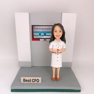 灰白色辦公背板前的CFO主題人像公仔：長深色髮女性公仔穿白色襯衫式連身裙，腳踩棕色尖頭鞋，雙手握紅色筆微笑站立。身後嵌入式螢幕顯示藍灰色表格與儀表板介面。公仔立於灰色紋理底座，前方放置金屬色小名牌寫有「Best CFO」。背景為純白。