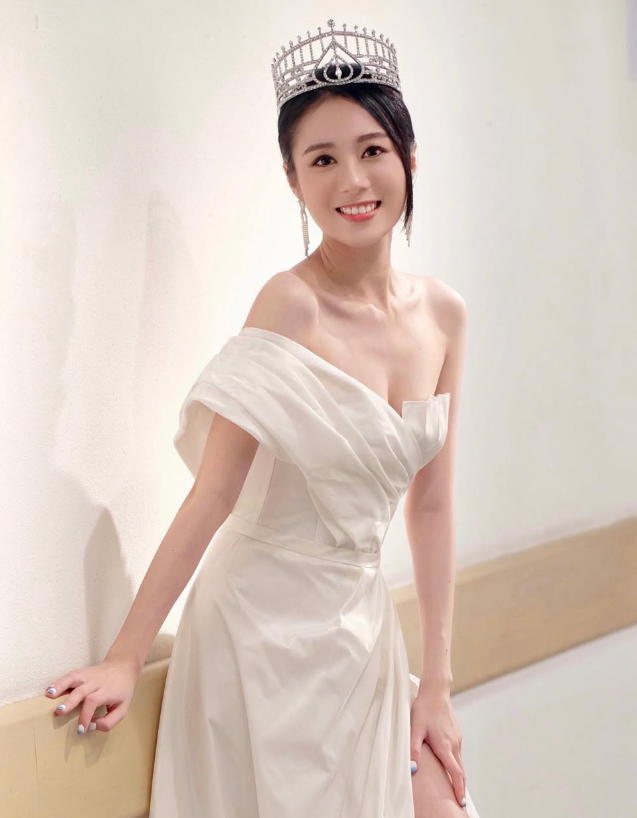 女子在室內拿著一個戴冠與綬帶的人像公仔，公仔穿亮片長裙站在白色底座上；畫面右下角或旁側疊有頒獎舞台的對比照片。